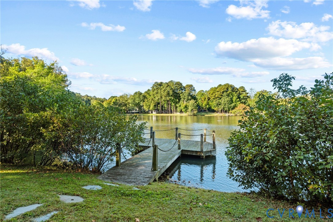 Waterfront property featuring a wooden pier with rope railing, manicured lawn, and mature trees
