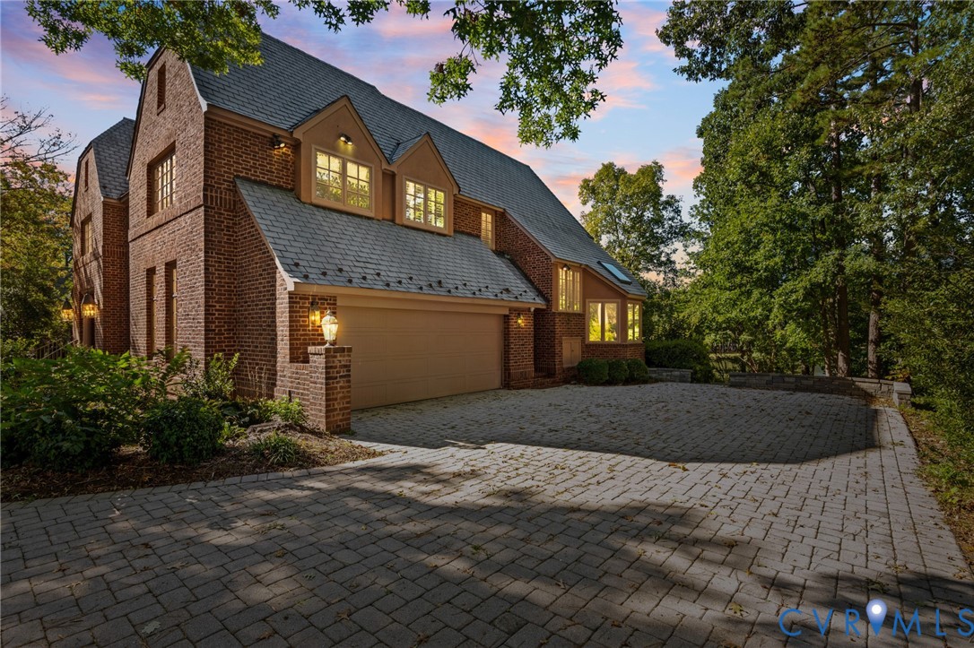 Multi-story brick exterior featuring a multi-gabled roofline, dormer windows, and a paved stone driveway