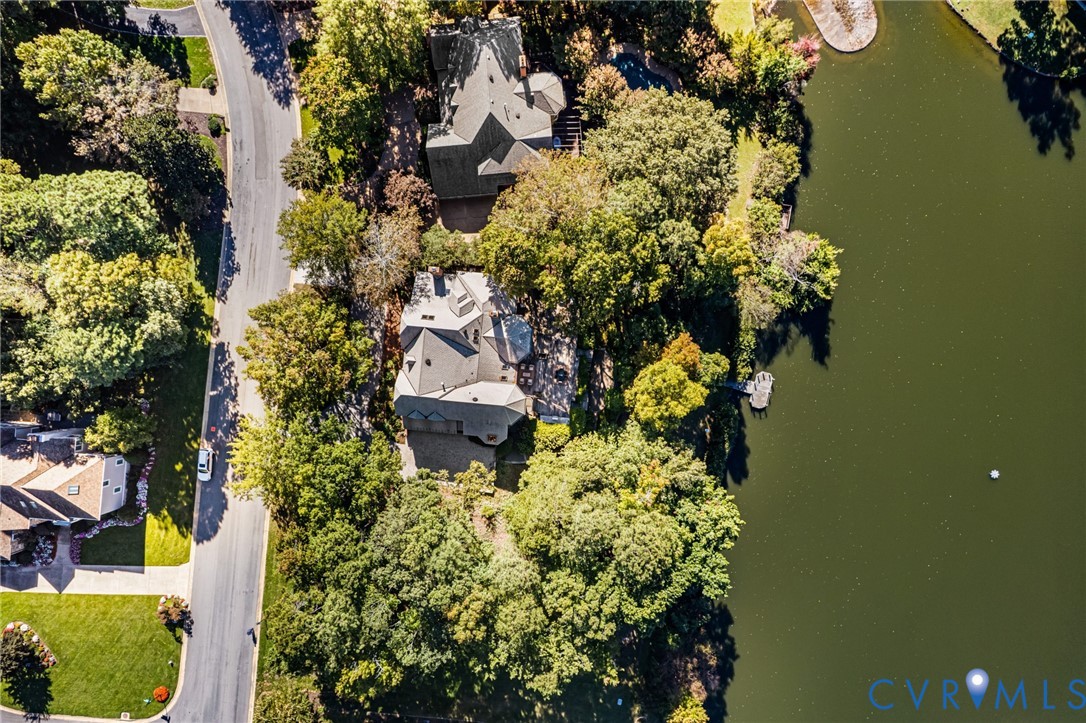 Aerial perspective featuring a multi-pitched roofline, paved driveway, mature wooded canopy, and private shoreline access to the water