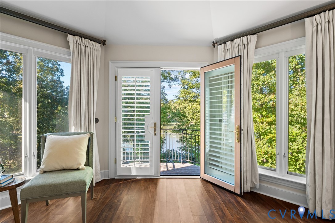 Multi-paneled bay windows, wood-finish flooring, and glass-paneled exterior door opening to a balcony with metal railing