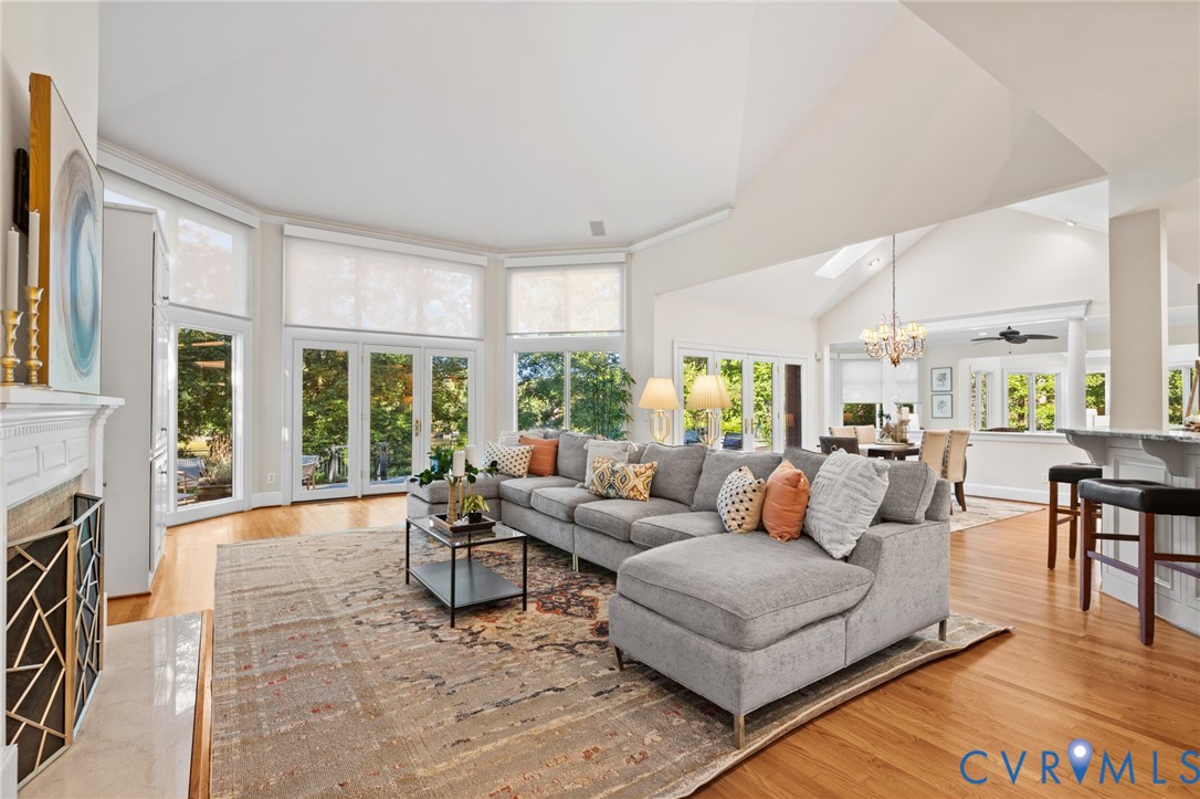 Vaulted ceilings, expansive windows with exterior glass doors, wood-finish flooring, and a fireplace with a decorative metal screen