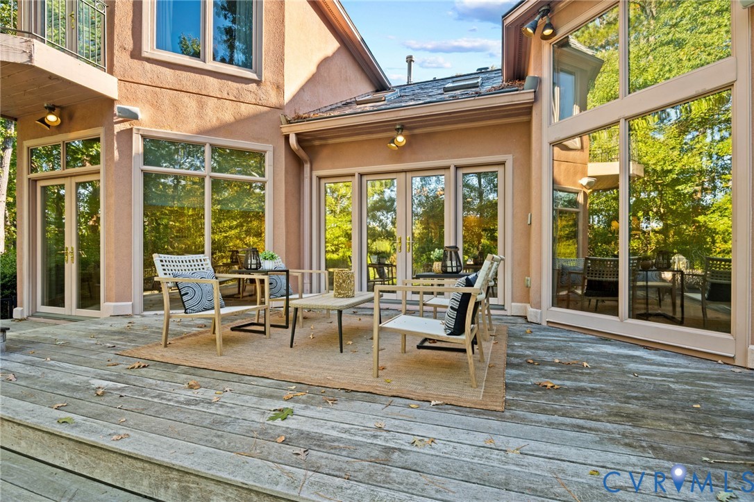 Stucco exterior featuring extensive floor-to-ceiling glass paneling, multiple sets of glass-paneled double doors, and a wood-decked outdoor patio