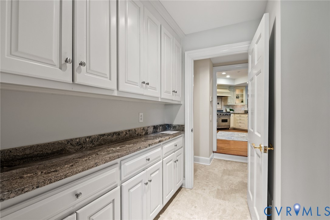 Custom white cabinetry featuring shaker-style doors, natural stone countertop, tile flooring, and a six-panel interior door