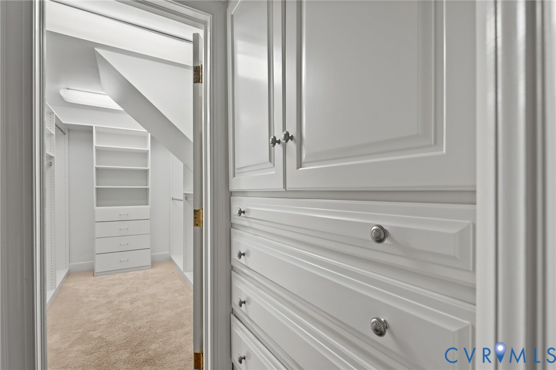 Custom walk-in storage featuring white cabinetry with raised-panel doors, integrated drawer banks, adjustable shelving, and carpet flooring