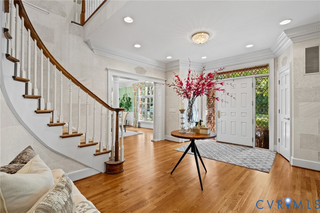 Foyer featuring curved staircase with wood handrail, hardwood flooring, crown molding, recessed lighting, and front door with leaded glass sidelights