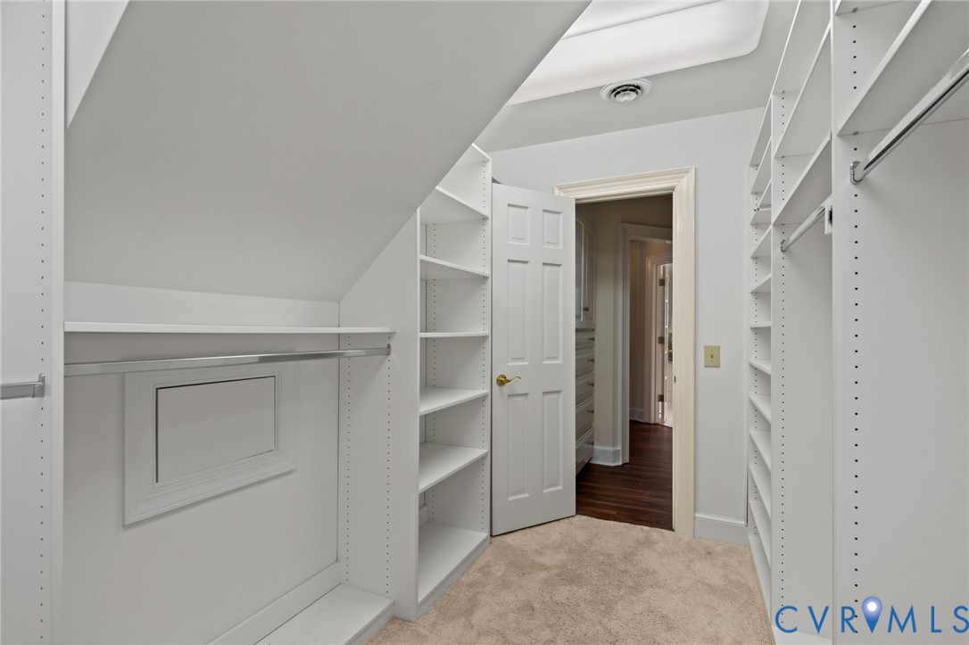 Custom walk-in closet featuring floor-to-ceiling white shelving, adjustable hanging rods, and integrated skylight lighting