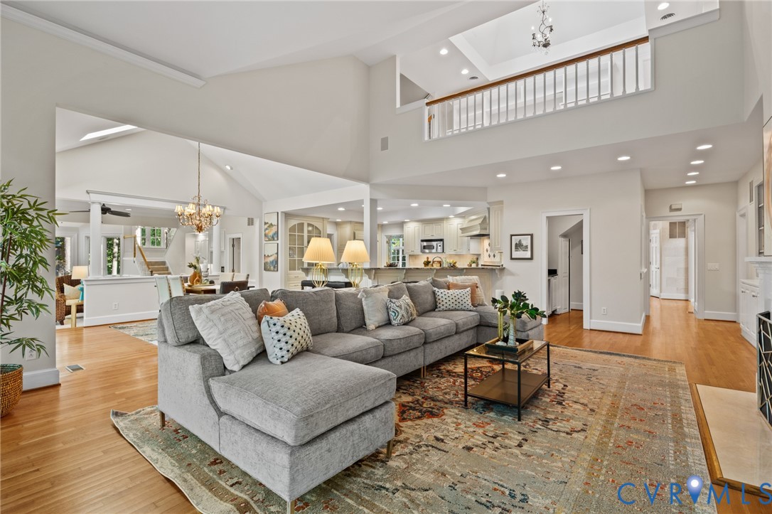 Open-concept interior featuring vaulted ceilings, wood-finish flooring, a mezzanine balcony with a wooden railing, recessed lighting, and a crystal chandelier