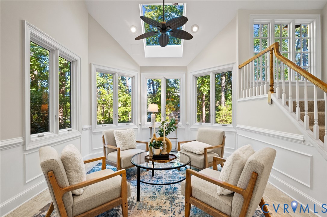 Vaulted ceiling featuring a central skylight, multi-pane windows, wainscoting, and a wooden handrail with balusters