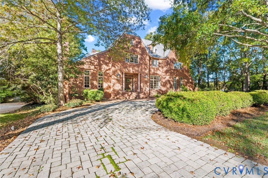 Two-story brick exterior featuring a steeply pitched roofline, multi-pane windows, and a paved stone driveway