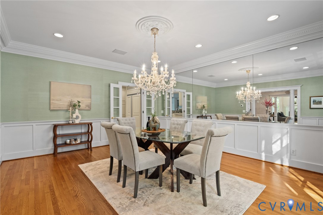 Formal dining space featuring intricate crown molding, extensive wall wainscoting, polished wood-finish flooring, a crystal chandelier with a decorative ceiling medallion, and a large-scale wall mirror