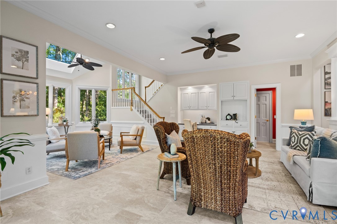 Open-concept interior featuring large-format tile flooring, recessed lighting, built-in cabinetry, a multi-paneled staircase with a wooden handrail, and oversized windows with a transom