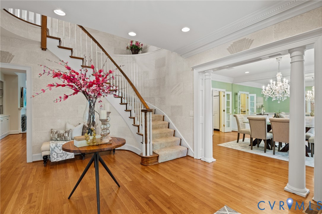 Foyer featuring a curved staircase with a wood handrail, hardwood flooring, recessed lighting, crown molding, and columns