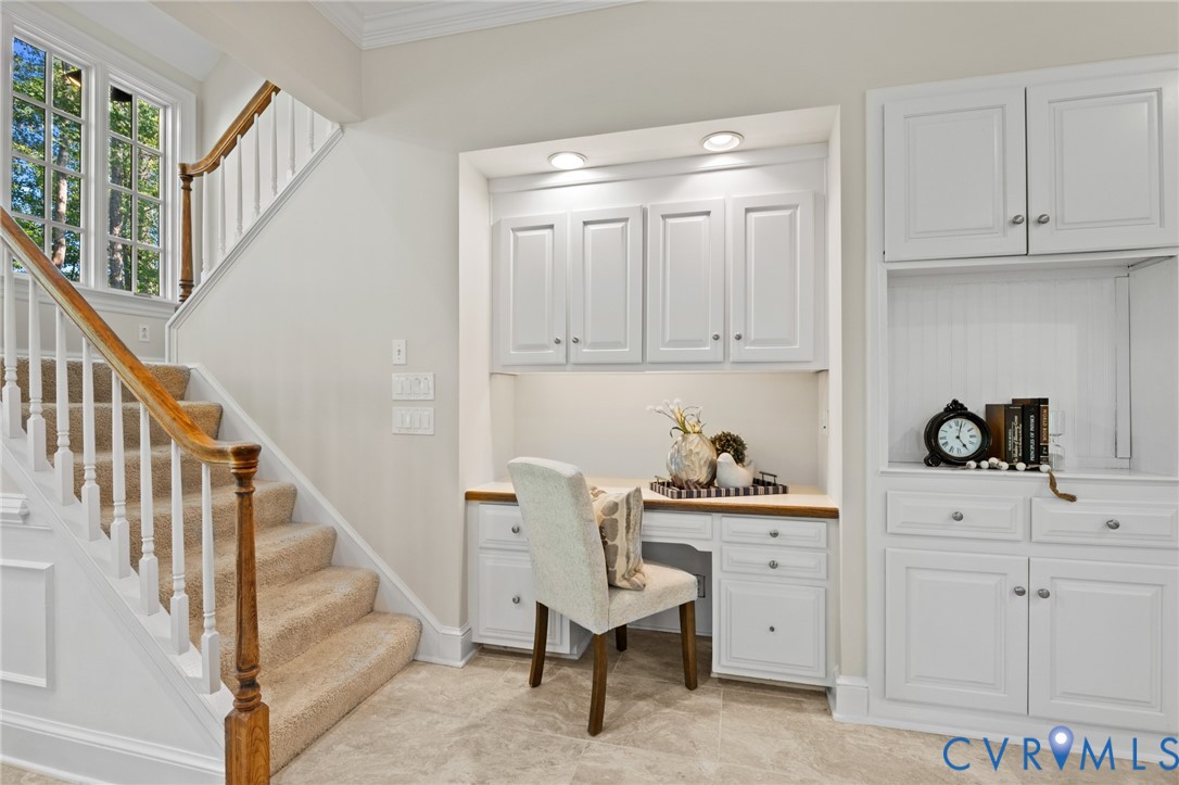 Built-in white cabinetry featuring recessed-panel doors, solid surface desk workspace, integrated recessed lighting, and staircase with wood handrail