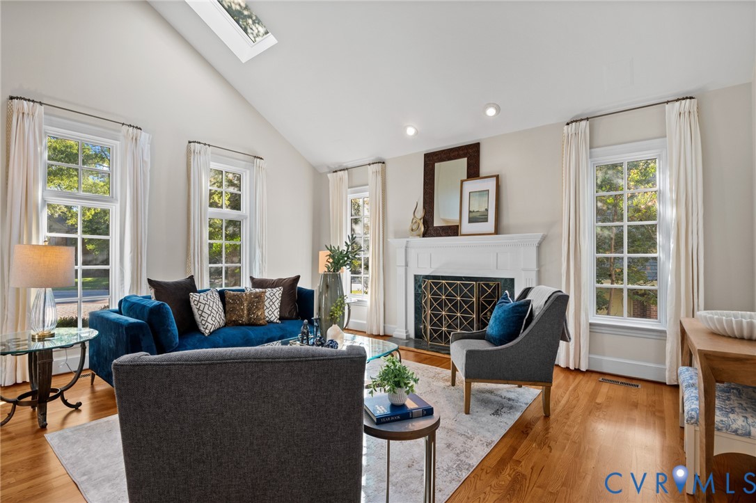 Living area featuring a vaulted ceiling with a skylight, wood-finish flooring, and a fireplace with a decorative mantel and surround