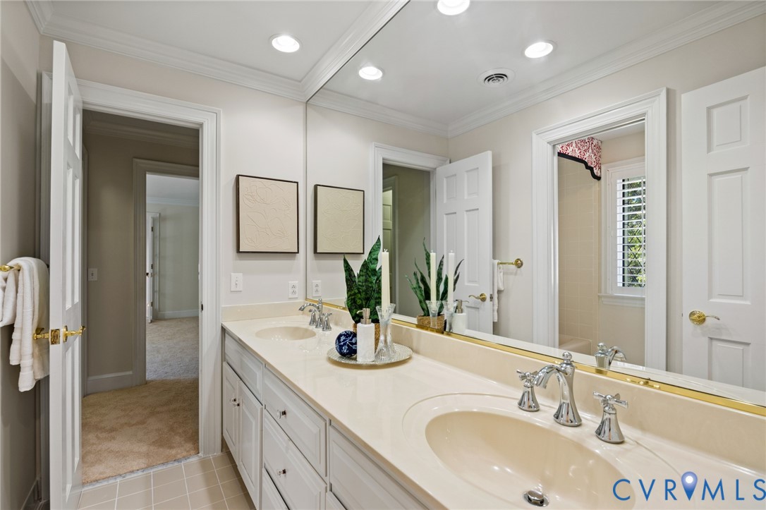 Double-sink vanity featuring a solid-surface countertop, integrated oval basins, polished chrome fixtures, and white shaker-style cabinetry with crown molding