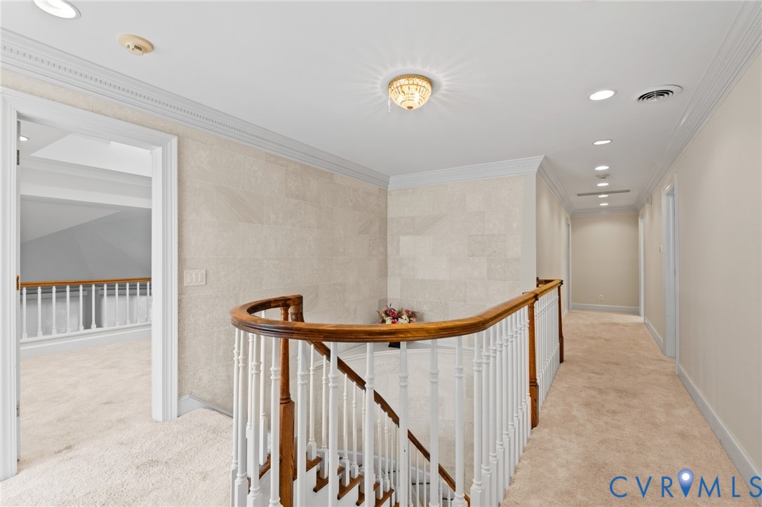 Curved staircase featuring a wooden handrail and white balusters, stone-tile accent wall, crown molding, and recessed lighting