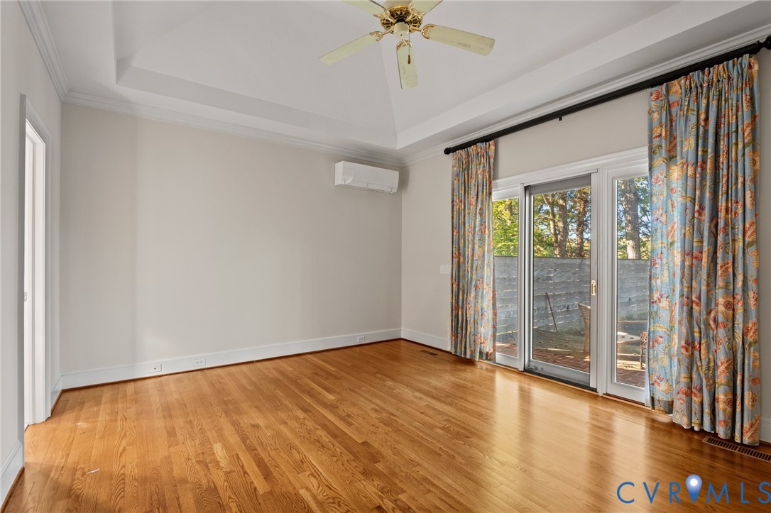 Tray ceiling with crown molding, wood-finish flooring, wall-mounted ductless HVAC unit, ceiling fan, and sliding glass doors