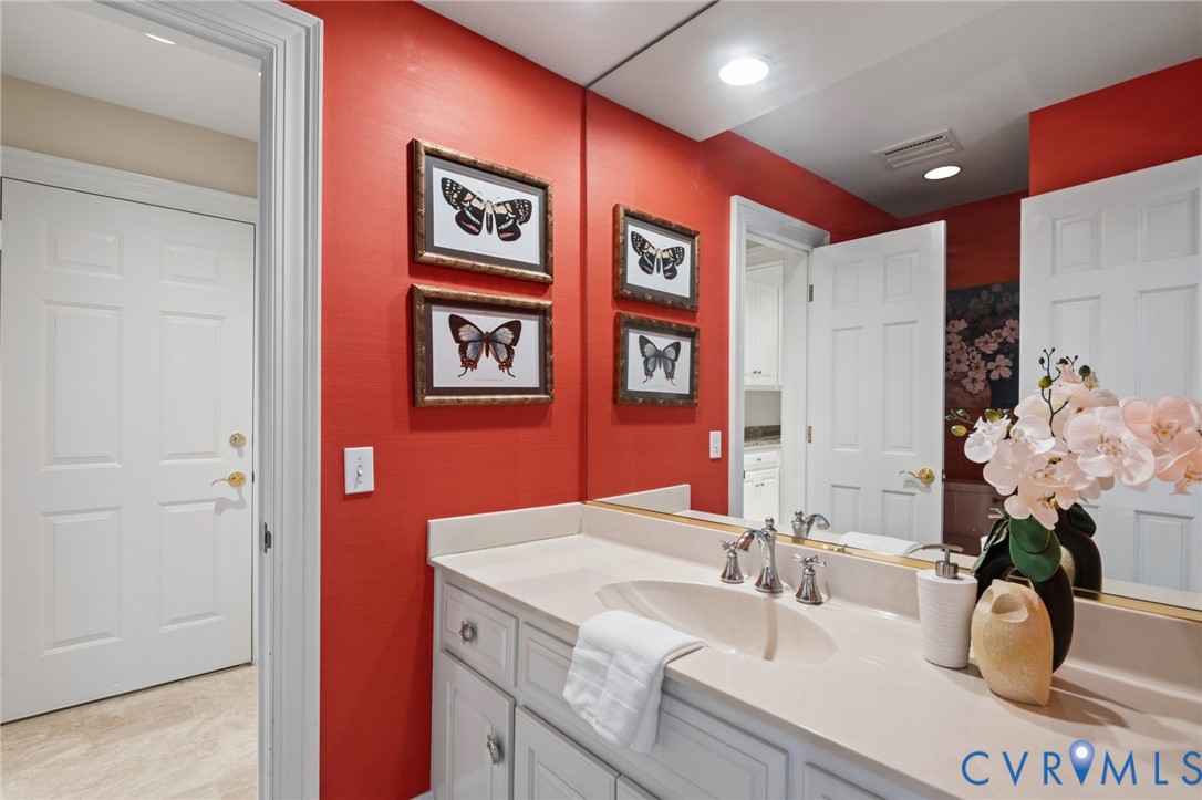 White cabinetry featuring polished metal hardware, integrated vanity with a molded basin, quartz countertop, and full-width wall mirror