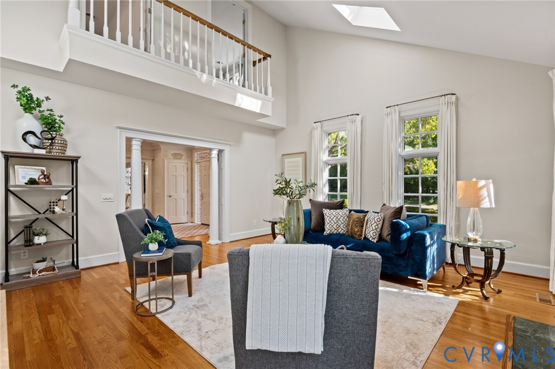 Vaulted ceiling featuring a skylight, wood-finish flooring, and a second-level railed gallery with white balusters and wood handrail