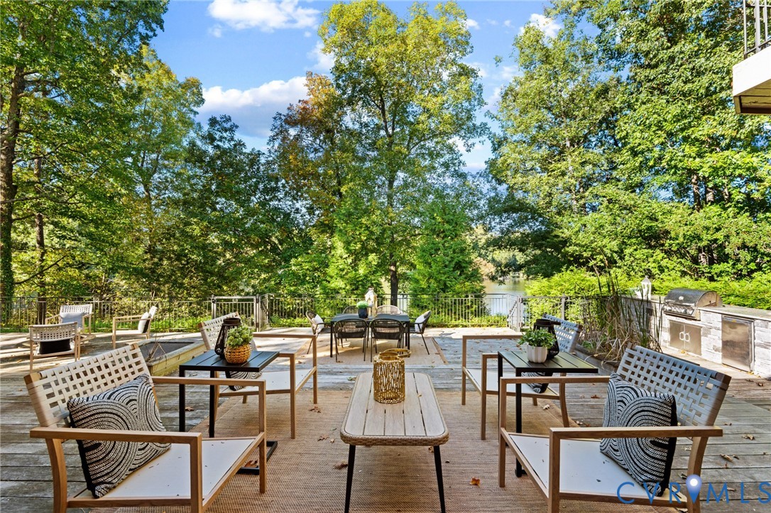 Expansive outdoor deck featuring a built-in stone grill station, metal perimeter fencing, and mature trees