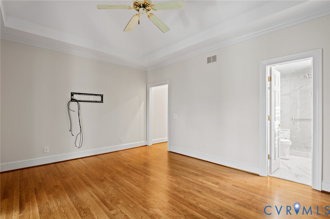 Room featuring tray ceilings, wood-finish flooring, and a ceiling fan with integrated lighting