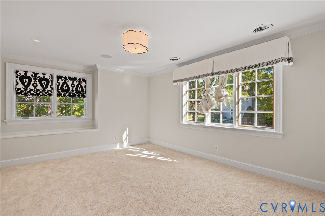 Neutral-toned interior featuring multi-pane windows, crown molding, wall-to-wall carpeting, and a flush-mount scalloped light fixture