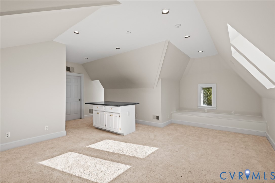 Vaulted ceiling with recessed lighting, skylights, built-in lower cabinetry with a stone countertop, and custom recessed window seating
