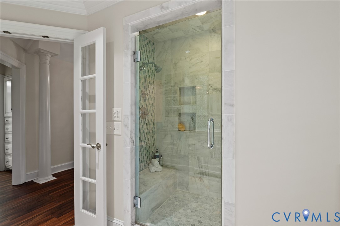 Walk-in shower featuring a glass door, stone-tile surround, built-in bench seating, mosaic accent wall, and recessed shelving