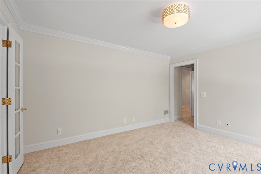 Neutral-toned room featuring crown molding, carpeting, a decorative flush-mount ceiling light fixture, and a French door with glass paneling
