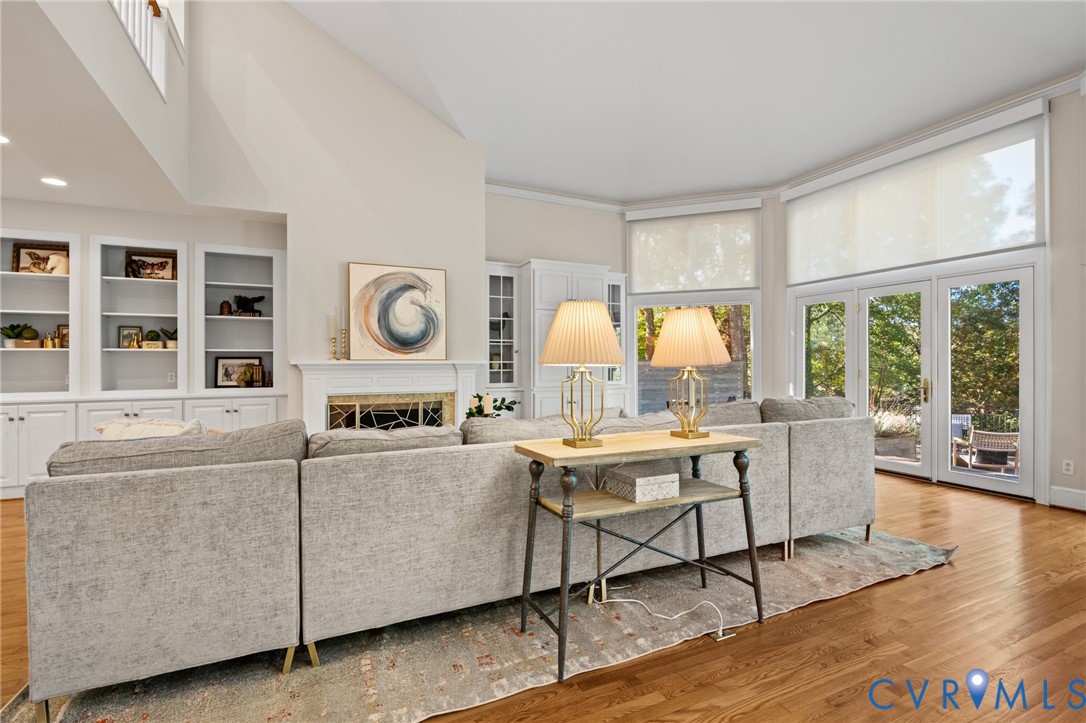 Vaulted ceiling with expansive windows, wood-finish flooring, floor-to-ceiling built-in cabinetry, and a fireplace with a decorative metal screen