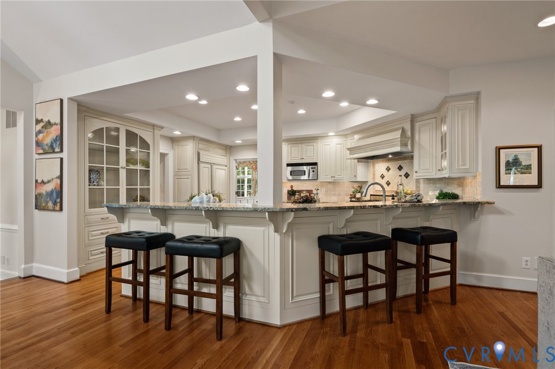 Kitchen featuring custom cabinetry, a stone-surfaced breakfast bar, recessed lighting, wood-finish flooring, and a built-in china display cabinet