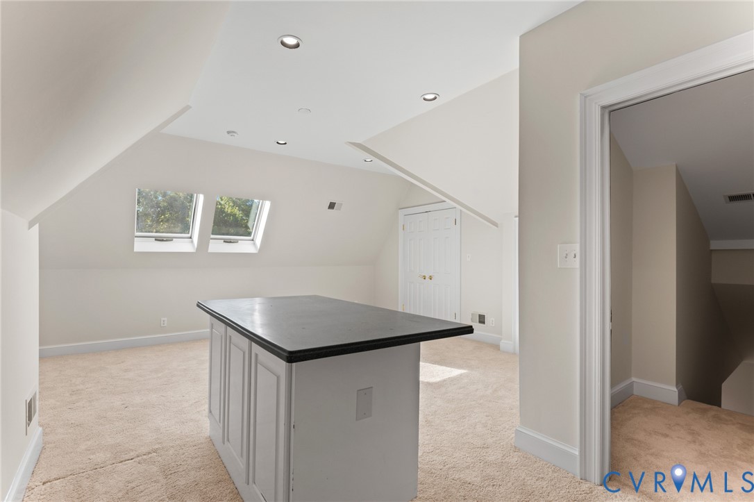 Vaulted ceiling with recessed lighting, skylights, central island with dark countertop, and built-in closet storage