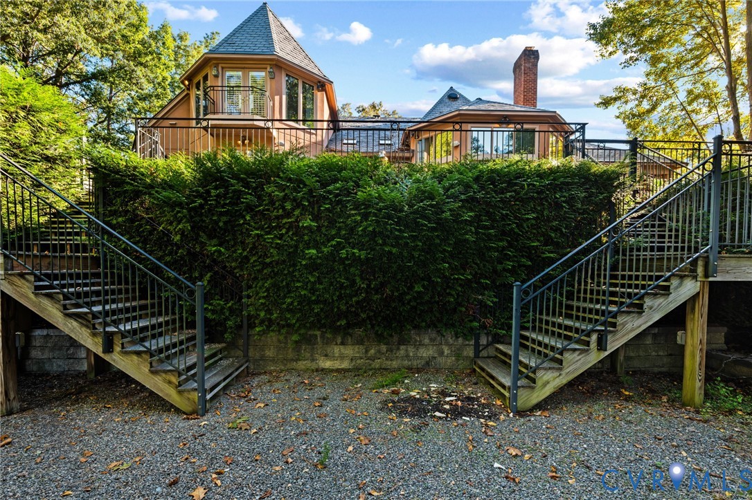 Exterior featuring multi-level rear decking with metal railings, dual wooden staircases, a turret-style roofline, and a stone retaining wall