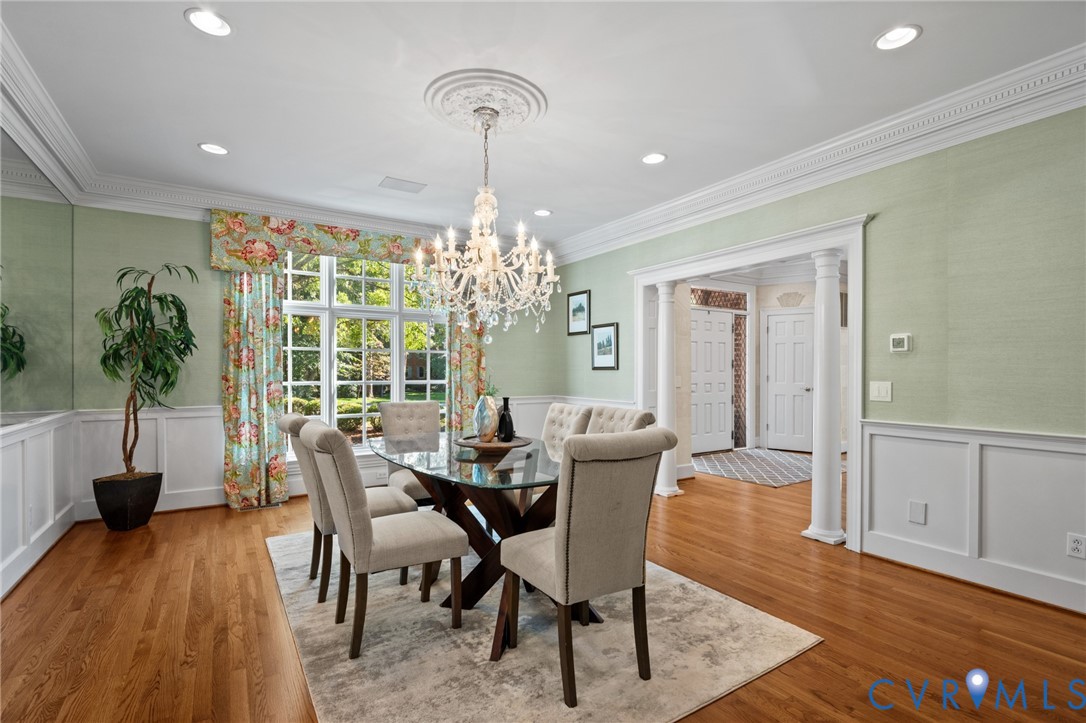 Dining room featuring hardwood flooring, wainscoting, an ornate ceiling medallion, crystal chandelier, and classical columns