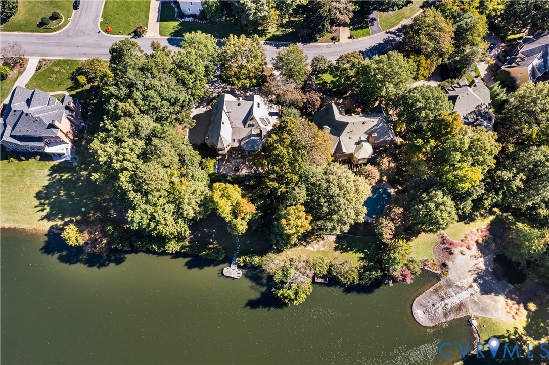 Aerial perspective of a multi-level residence featuring a shoreline position, a private dock, an in-ground swimming pool, and mature wooded landscaping
