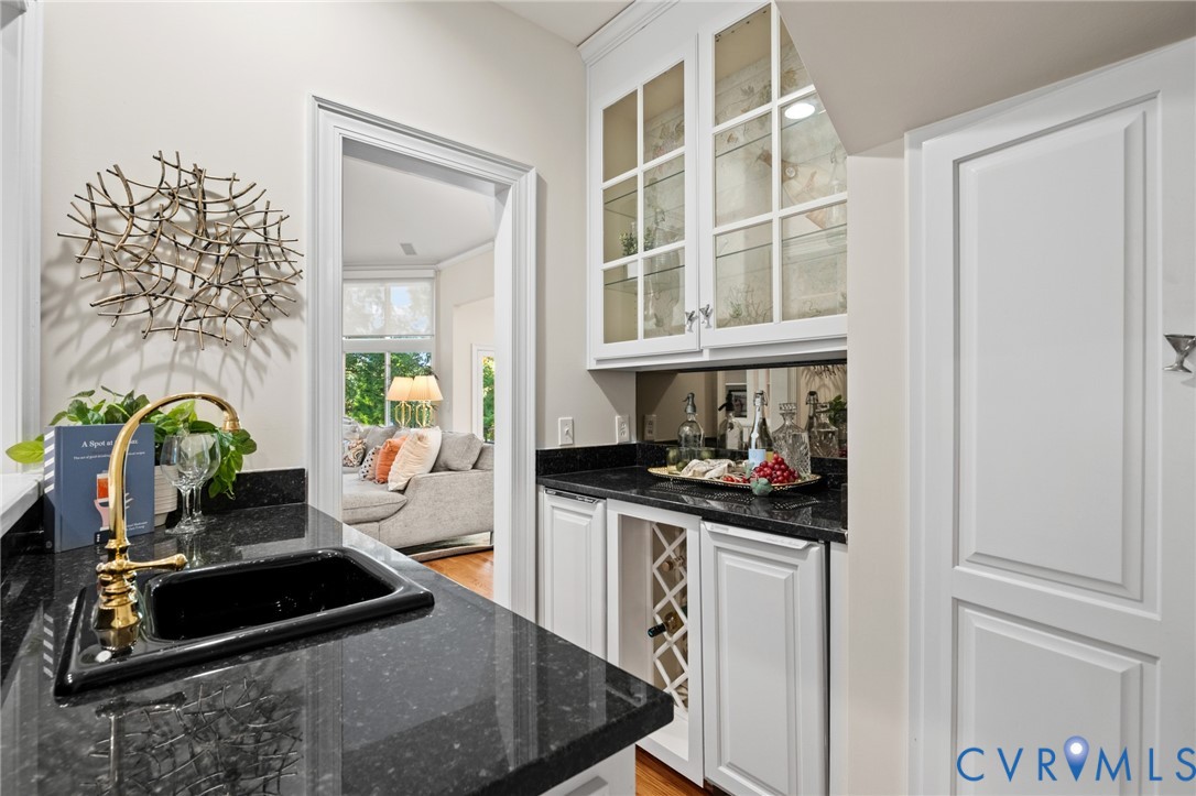 Wet bar featuring dark stone countertops, custom white cabinetry, a built-in wine rack, glass-front upper cabinet doors, and a gold-toned faucet