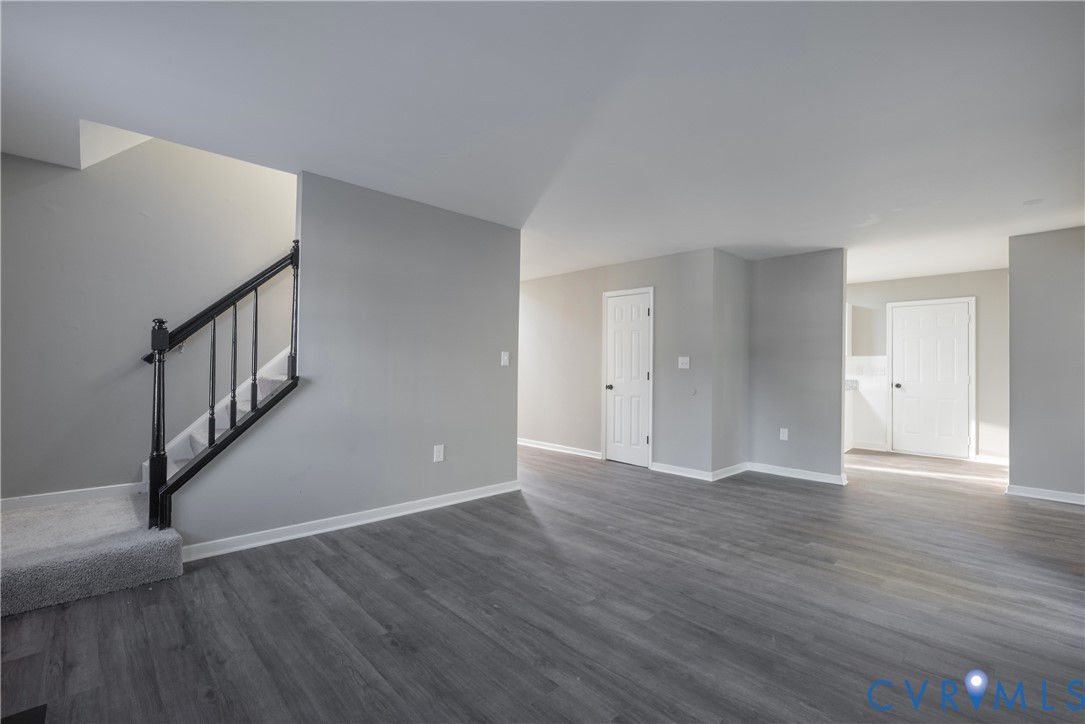 Open-concept with new flooring, neutral wall paint, and a staircase with a black handrail and balusters
