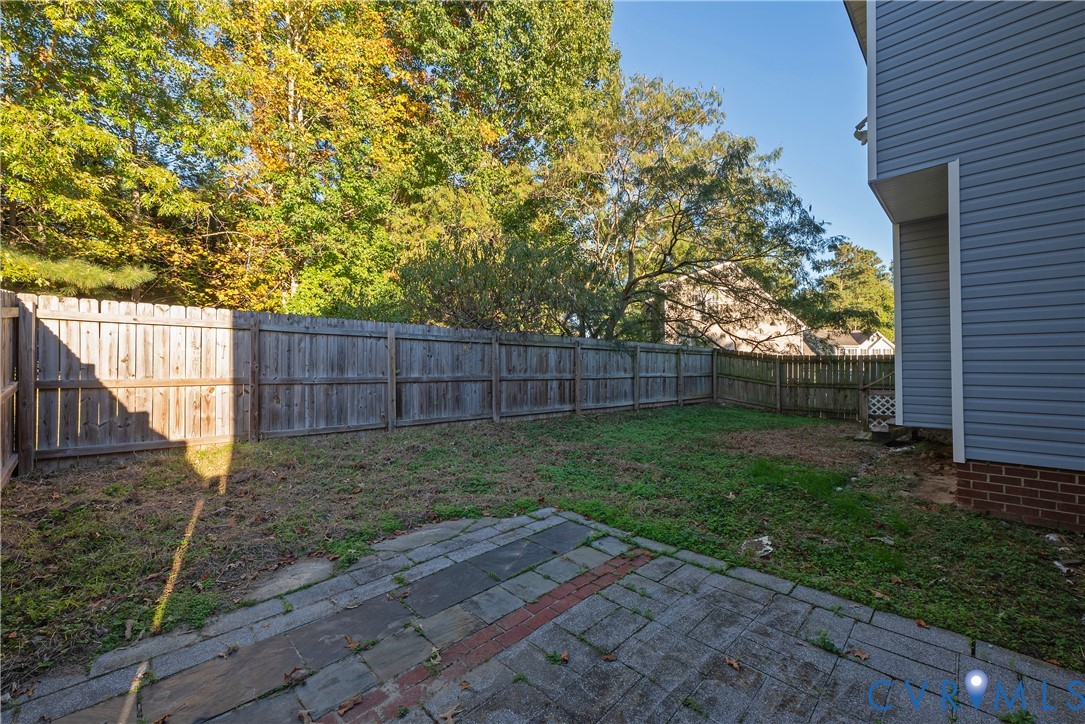 Backyard featuring a stone paver patio, wood privacy fencing, and exterior vinyl siding with brick foundation detail