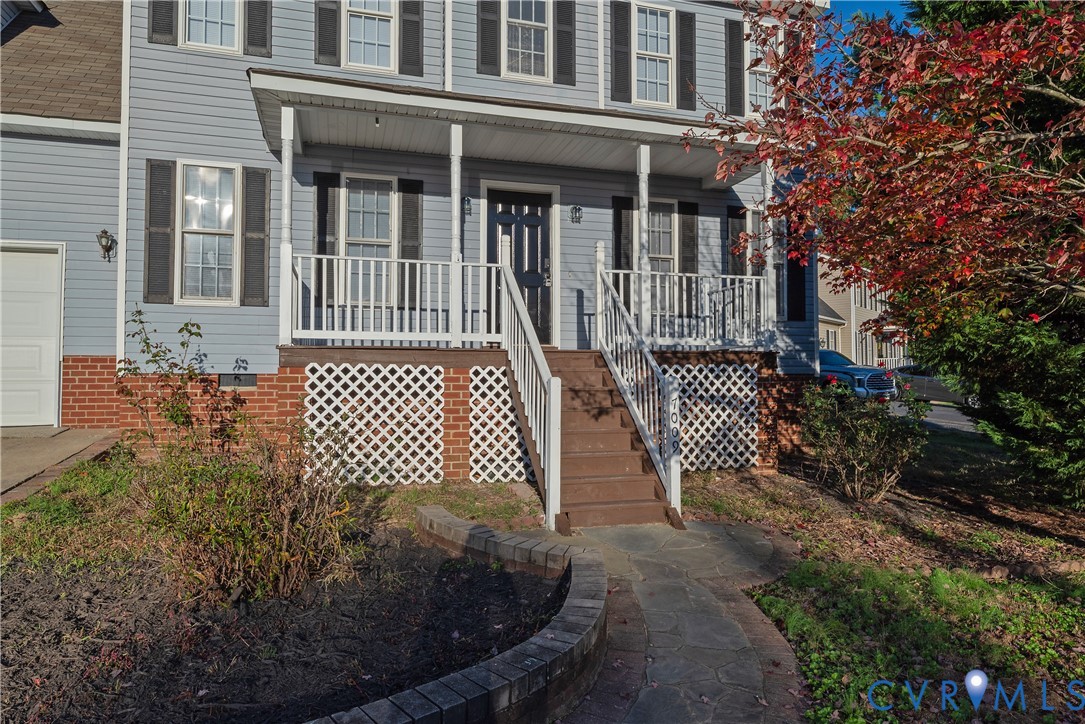 Colonial-style exterior featuring lap siding, a covered front porch with white railing, brick foundation skirting, decorative lattice panels, and a stone walkway