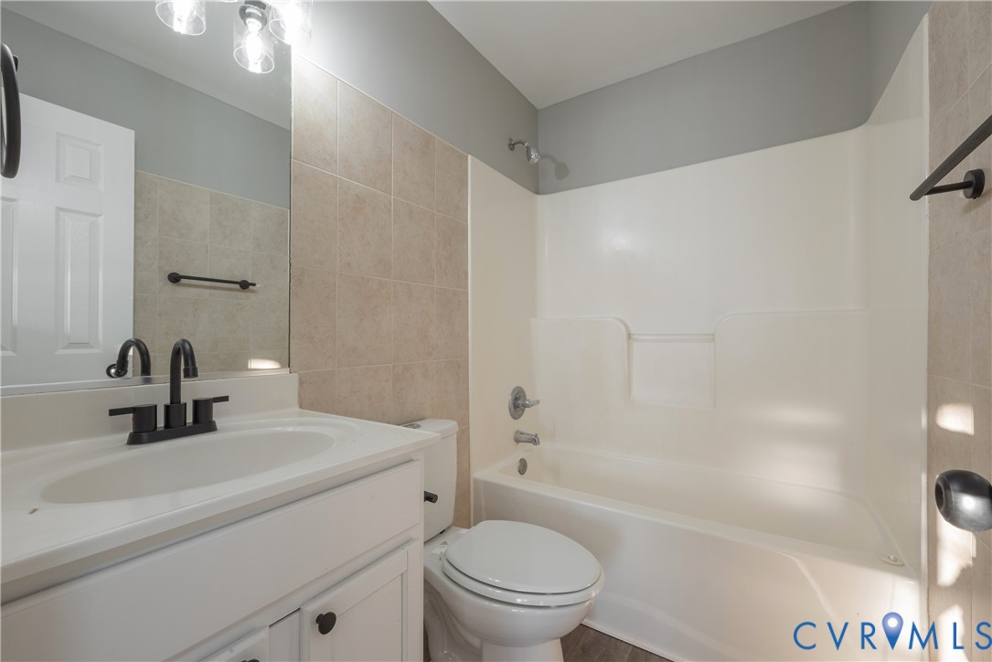 Hall bathroom featuring a white vanity with a rectangular sink, matte black faucet, wall-mounted mirror with integrated lighting, and a neutral tile surround tub-shower combination