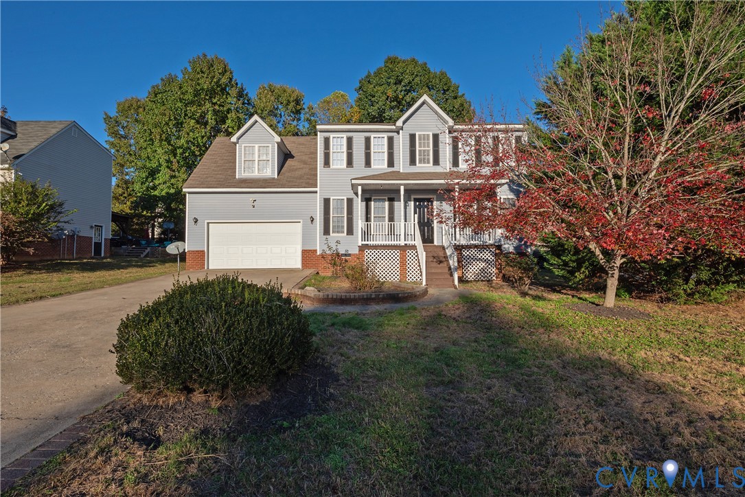Two-story home with light blue siding, decorative shutters, a covered front porch, integrated two-car garage, and a brick-accented foundation