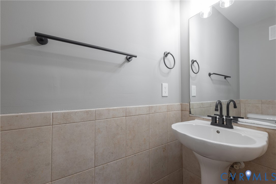 Powder Room Pedestal sink with a matte black faucet, wall-mounted mirror, ceramic tile wainscoting, and matte black towel hardware