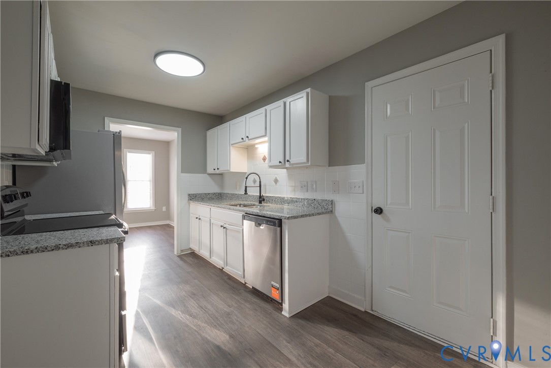 Kitchen featuring white shaker-style cabinetry, granite countertops, a stainless steel dishwasher, a high-arc matte black faucet, and wood-finish flooring and backsplash