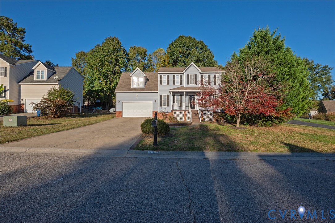 Two-story colonial exterior featuring vinyl siding, a covered front porch, decorative window shutters, an attached two-car garage, and a concrete driveway