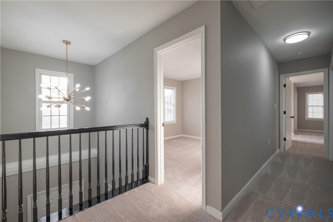 Upper Hallway looks over a 2 Story Foyer with spindle railing, multi-arm sputnik-style chandelier, neutral carpeting, and multi-pane windows