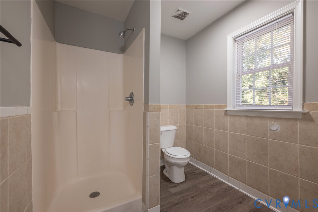 Bathroom featuring a walk-in shower with integrated surround, dual-toned wall tile wainscoting, wood-finish flooring, and a window with blinds