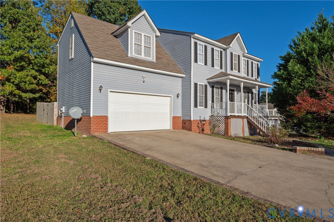 Two-story residence featuring light-blue vinyl siding, a red brick foundation, an attached two-car garage, a covered front porch with railing, and multi-pane windows with shutters
