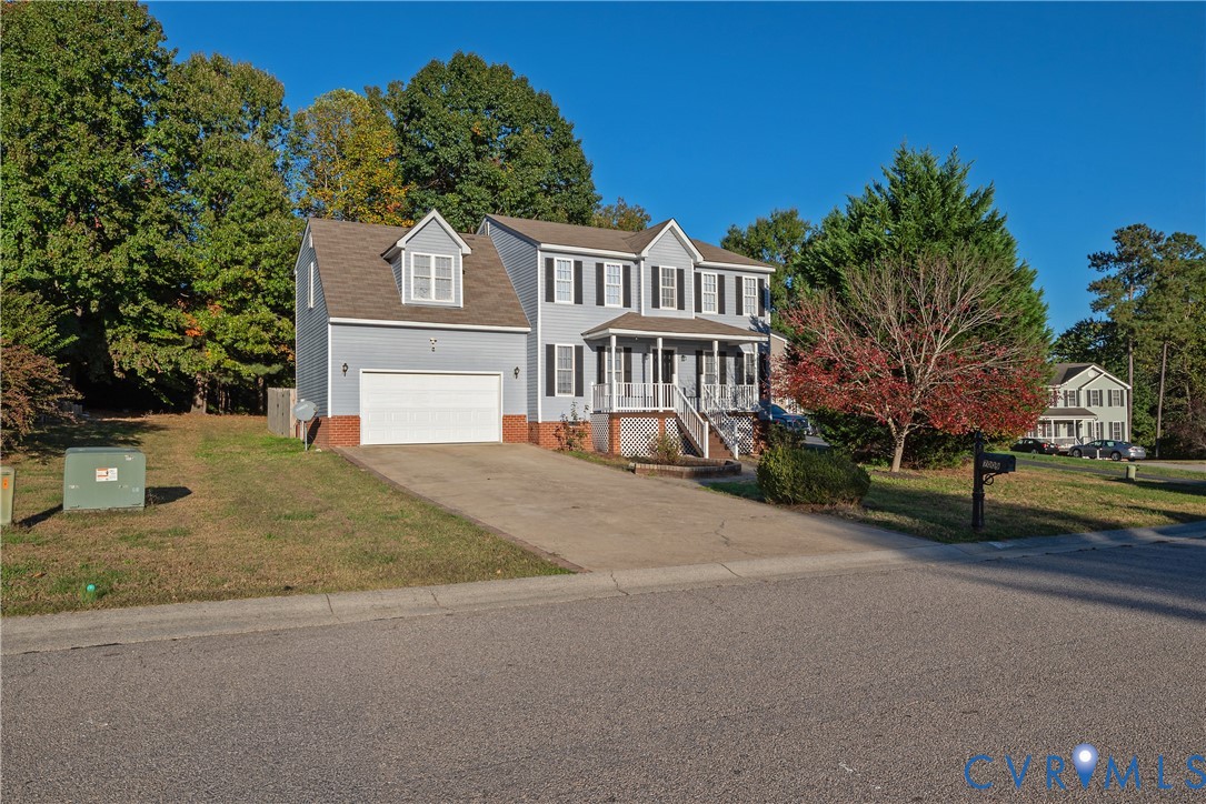 Two-story residence featuring a front porch with a white railing, a double-car garage, brick veneer accents, and an expansive lawn