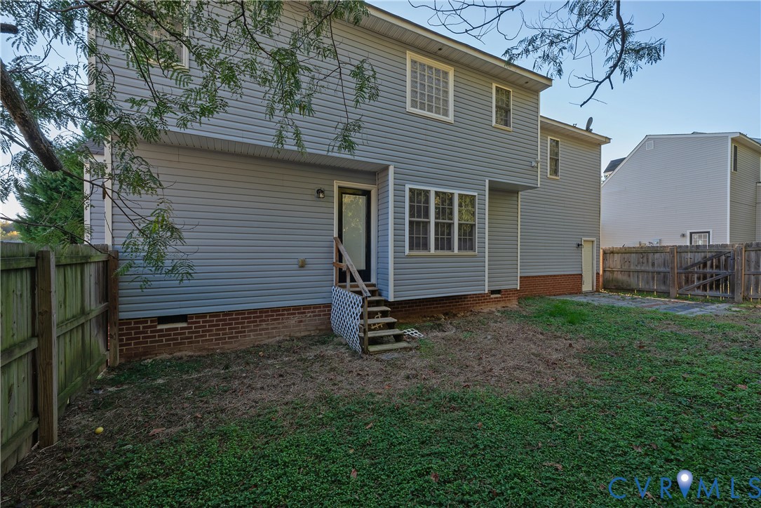 Rear exterior featuring horizontal lap siding, brick foundation, multi-pane windows, and a wood staircase leading to a rear entrance, enclosed by wood privacy fencing