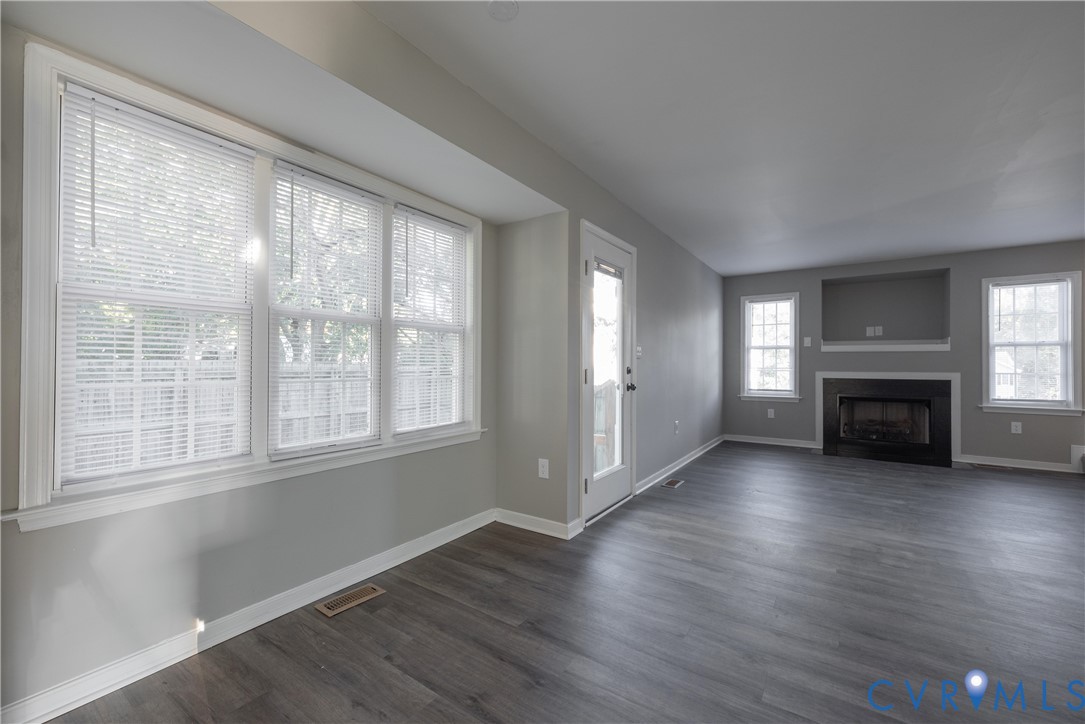 Family Room area featuring new flooring, a fireplace with a black surround, recessed media niche, multiple windows, and a glass-paneled exterior door
